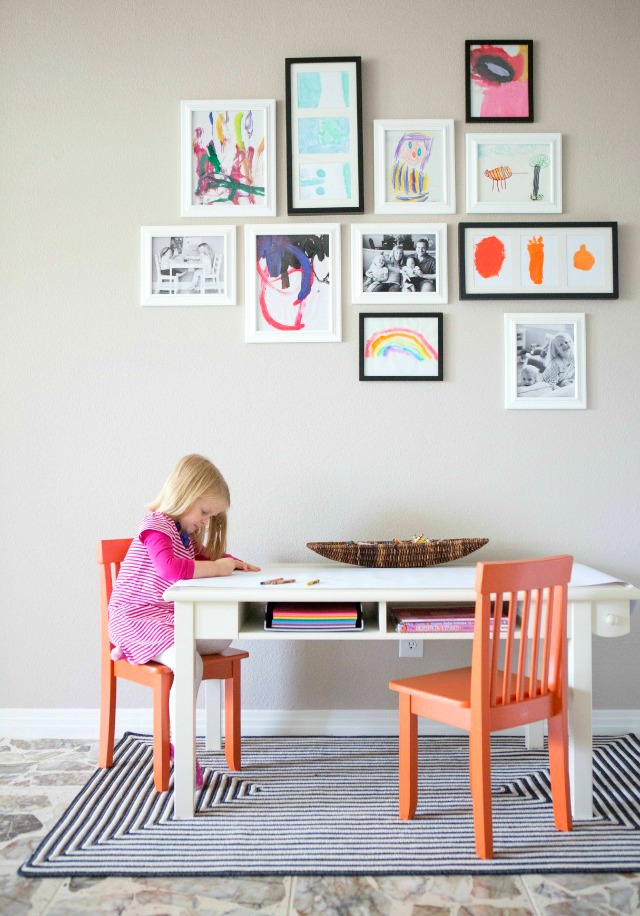 Gallery wall of kids art with child working at table below