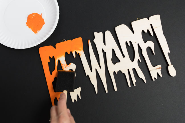 Painting wood Beware sign with orange paint